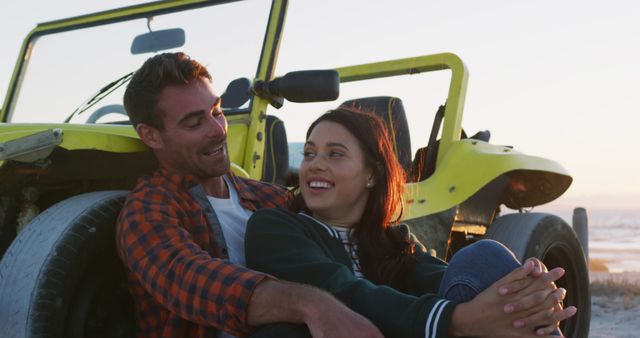 Couple enjoying sunset by the beach, seated with a yellow dune buggy. Ideal for themes about love, relaxation, vacation, travel, adventure, and outdoor activities.