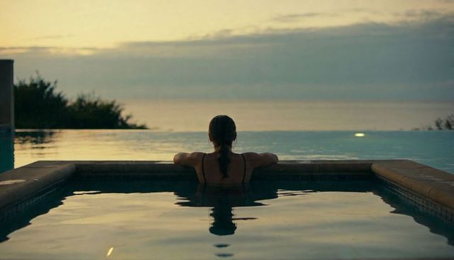 Woman relaxing at infinity pool facing ocean horizon at twilight