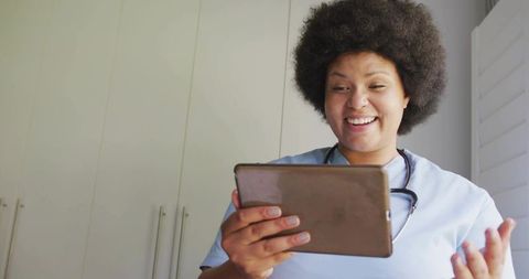 Smiling nurse conducting telehealth consultation on tablet, wearing scrubs and stethoscope
