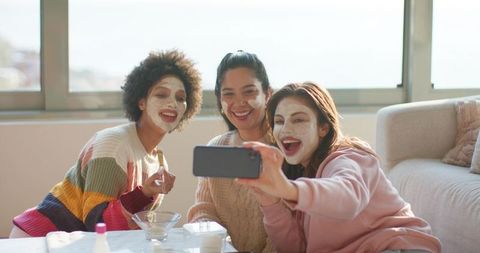 Friends taking selfie during at-home skincare party, diverse women wearing face masks