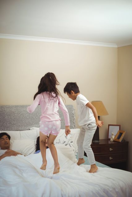 Siblings jumping on bed in bedroom at home