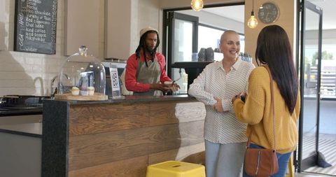 Customers chatting at cozy cafe counter while barista preparing drinks and cupcakes