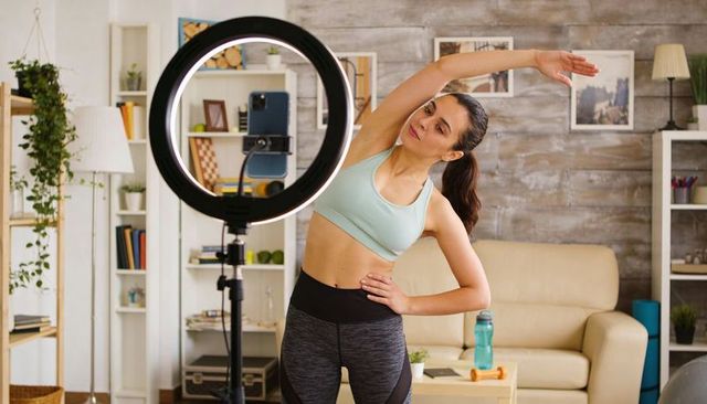 Female fitness creator stretching on camera with ring light and smartphone tripod workout
