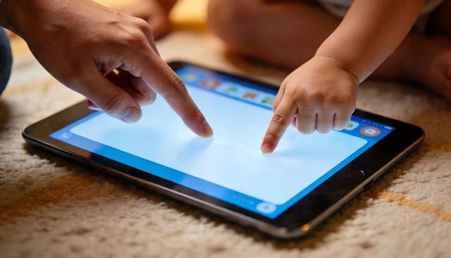 Adult and toddler touching tablet screen for shared learning and digital bonding