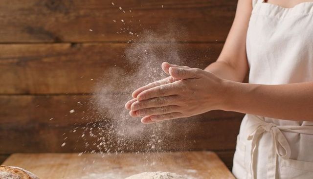 Baker clapping hands releasing flour cloud over floured countertop with dough and apron