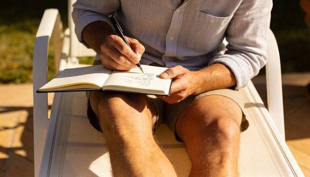 Man writing in notebook on sunlit patio chair journaling outdoors relaxing backyard morning