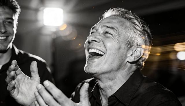 Mature man laughing at celebration, black and white candid portrait with spotlight flare