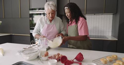 Senior Woman Teaching African American Woman Baking Mixing Batter in Modern Kitchen