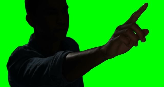 Silhouette figure pointing with hand extended against green screen backdrop. Useful for creating visual effects, digital editing, marketing promotions, advertising materials, and easily isolating and inserting new backgrounds.