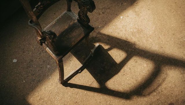 Antique carved wooden rocking chair casting dramatic shadow on sunlit dusty attic floor