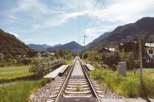 Perfect for promoting rural travel destinations, this captivating scene showcases a rail track winding through a picturesque village set against hills and greenery. Ideal for use in marketing travel brochures, outdoor adventure advertisements, and nature-oriented digital content.