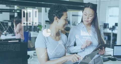 Collaborating female colleagues reviewing tablet with data dashboards and HUD analytics