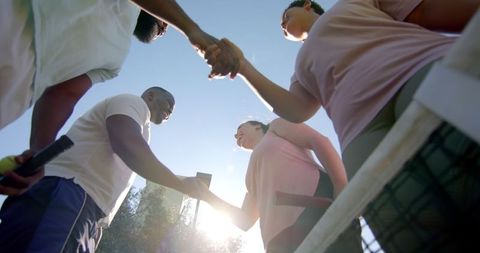 Diverse friends shaking hands on sunny tennis court