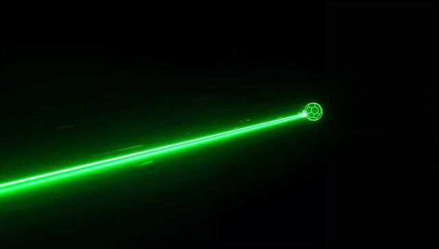 Slicing neon green laser beam cutting across black space toward glowing wireframe sphere