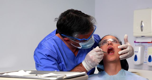 A middle-aged dentist is examining the teeth of a young female patient in a dental clinic, with copy space. Dental check-ups are crucial for maintaining oral health and preventing future dental issues.