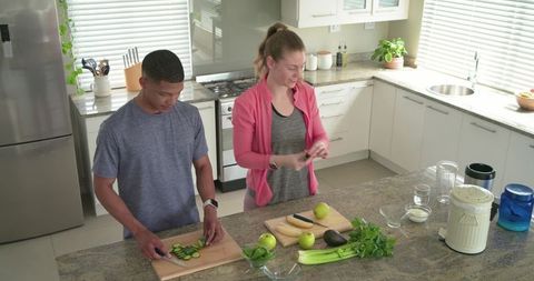Diverse couple preparing healthy meal, chopping vegetables on modern kitchen island