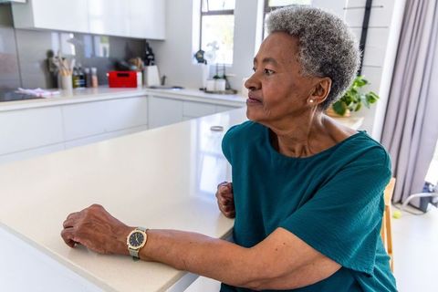 Senior african woman sitting contemplative at modern kitchen island wearing wristwatch