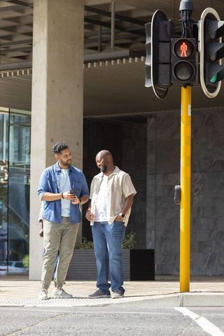 Two men chatting at crosswalk with smartphone under urban canopy near red pedestrian signal