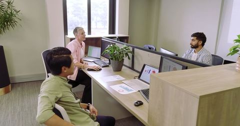 Diverse coworkers analyzing data in collaborative office cubicle