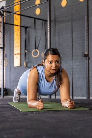 Woman holding forearm plank on mat in industrial gym building core strength and focus