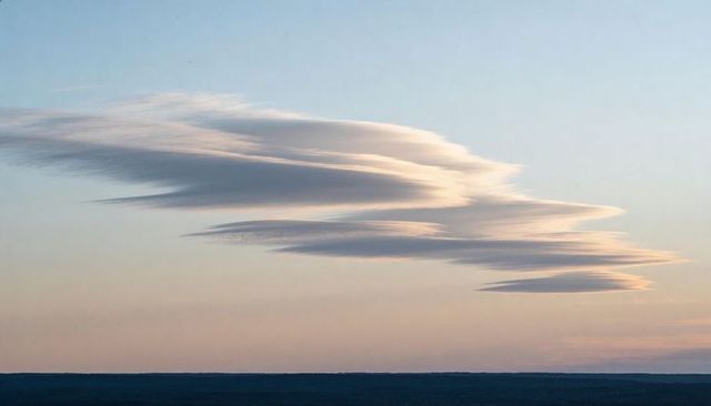 Layered lenticular clouds stretching over coastal horizon at sunrise