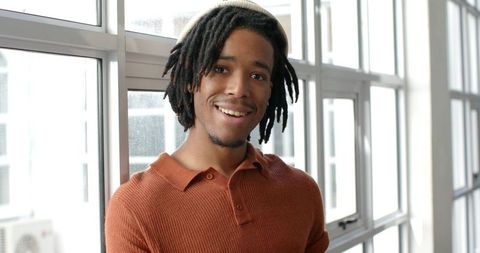 Smiling African American man leaning against windows in loft wearing rust sweater and headband
