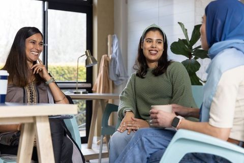 Multicultural women collaborating in bright coworking lounge sharing coffee and ideas
