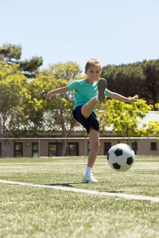Energetic young girl practicing soccer kick on sunlit grass field for youth sports training