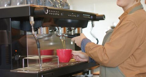 Female barista pulling espresso into red cups at commercial espresso machine