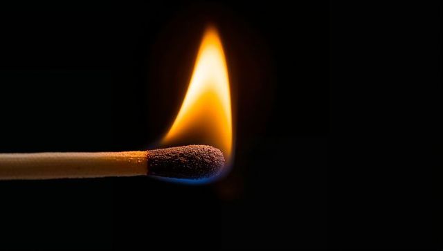 Burning single wooden matchstick producing vivid yellow-orange flame and glowing ember