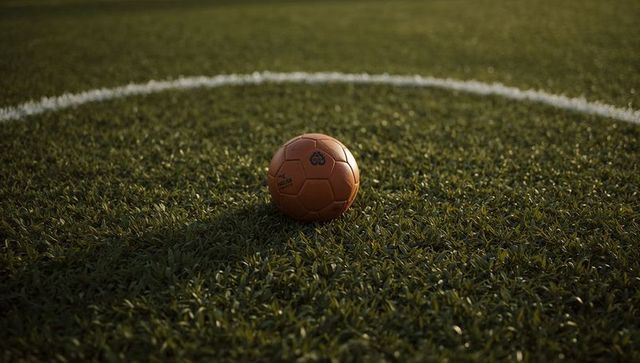 Orange soccer ball resting on center circle of sunlit artificial turf at golden hour