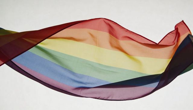 Translucent rainbow scarf floating in curved silk wave over neutral background