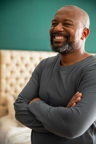 Mature african american man standing with arms crossed smiling in cozy bedroom warm lifestyle portra