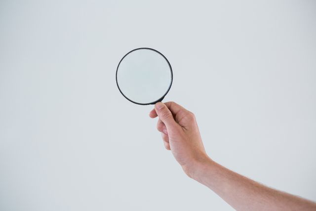 Hand holding magnifying glass against white background. Ideal for concepts related to searching, examining, investigation, and focus. Useful for educational materials, presentations, and articles on attention to detail.