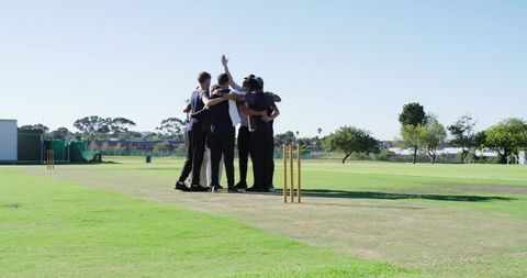 Huddling cricket team celebrating on sunny turf with stumps and helmet