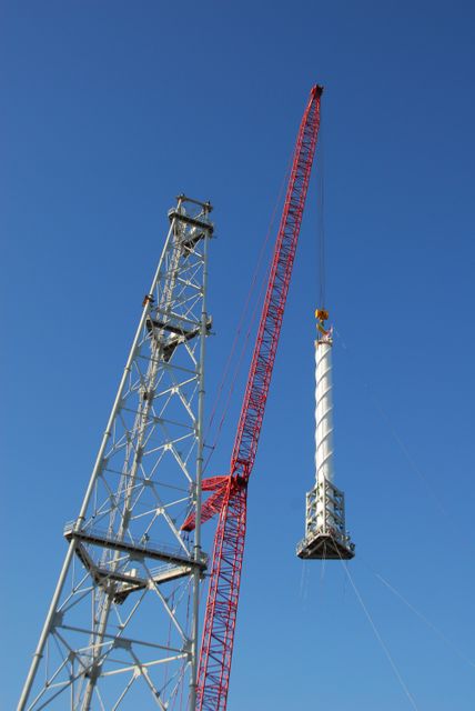 Crane lifting a 100-foot lightning mast at NASA's Kennedy Space Center Launch Pad 39B, alongside a towering new lightning protection structure. This installation is part of the Constellation Program preparing for the Ares I rocket launch. Ideal for illustrating technology, engineering and space exploration themes.