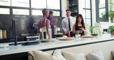 Multicultural coworkers chatting and sipping drinks at modern white kitchen island