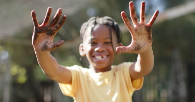 Happy african american boy standing, showing dirty hands and smiling in sunny vegetable garden. Nature, gardening, healthy life style, unaltered.