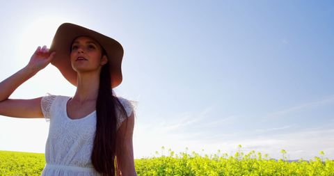 Happy young woman in white dress and hat in sunny mustard field