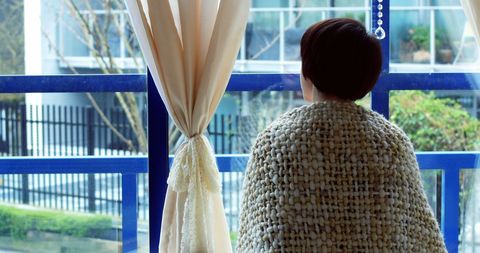 Middle-aged person in cozy blanket gazing out window on peaceful day