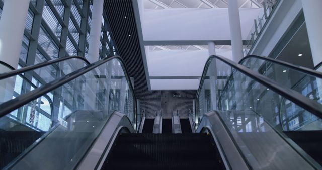 Escalators inside a modern commercial building, featuring sleek glass rails and contemporary design. Ideal for use in articles or advertisements related to architecture, urban development, commercial buildings, office spaces, travel, or business environments.