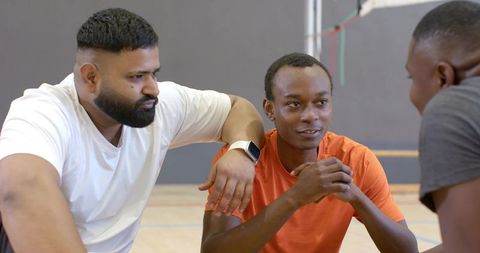 Diverse male teammates discussing strategy on gym court during basketball huddle with smartwatch