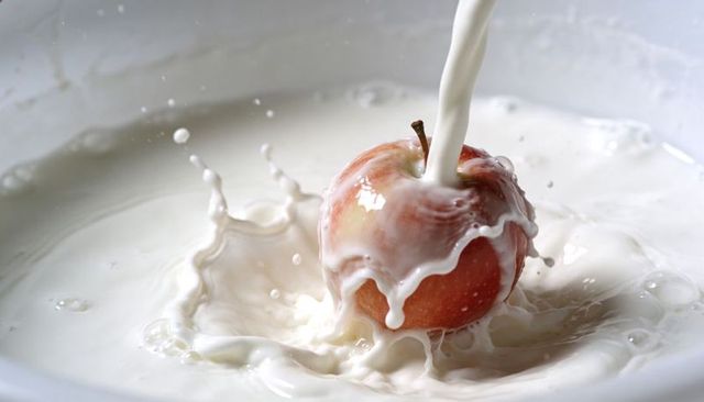 High-speed milk pouring over red apple creating crown splash with droplets and motion