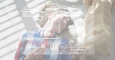 Young woman lying by window reaching for dog with futuristic augmented reality interface