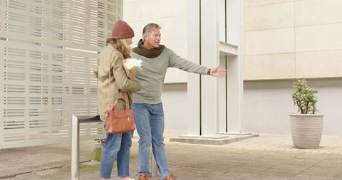 Senior couple meeting and greeting at urban plaza with bouquet and casual autumn style