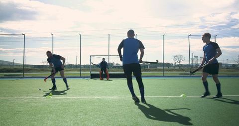 Male hockey players training with ball and sticks on artificial turf