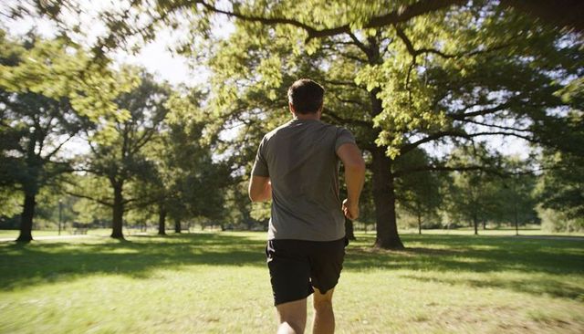 Male Runner Jogging Through Sunlit Park Trees Athletic Outdoor Workout