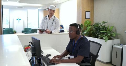 Receptionist wearing headset typing while doctor checks tablet at modern clinic desk