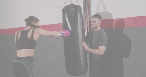 Woman punching heavy bag while coach steadying bag during boxing training session