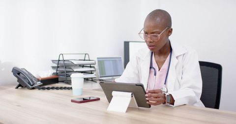 Clinician reviewing patient records on tablet at minimalist modern office desk wearing lab coat